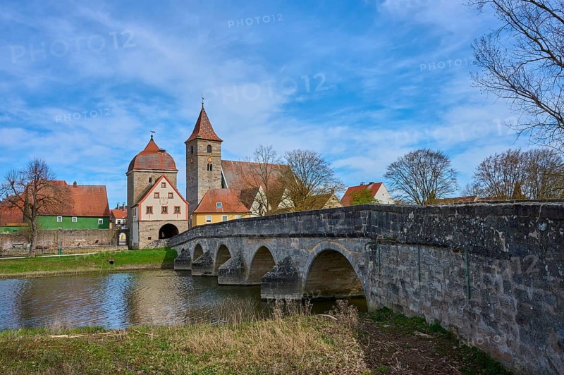 Historic stone bridge leads across river to a village with a distinctive church and towers, spring, Ornbau, Triesdorf, Franconian Lake District, Ansbach district, Middle Franconia, Bavaria, Germany