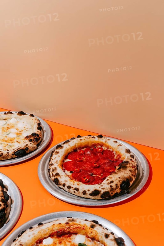 Wood-fired pepperoni pizza topped with salami, mozzarella, tomato sauce, and chili pepper. Served on a metal plate with a golden, crispy crust and rich, bold flavors
