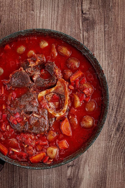 Ossobuco stew with vegetables, knuckle on the bone with new potatoes, in tomato sauce, homemade, top view, no people