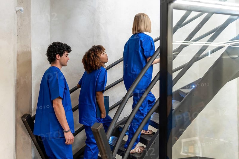 Diverse medical professionals in blue scrubs ascending a modern staircase, representing teamwork, career progression, and dedication within a contemporary healthcare environment