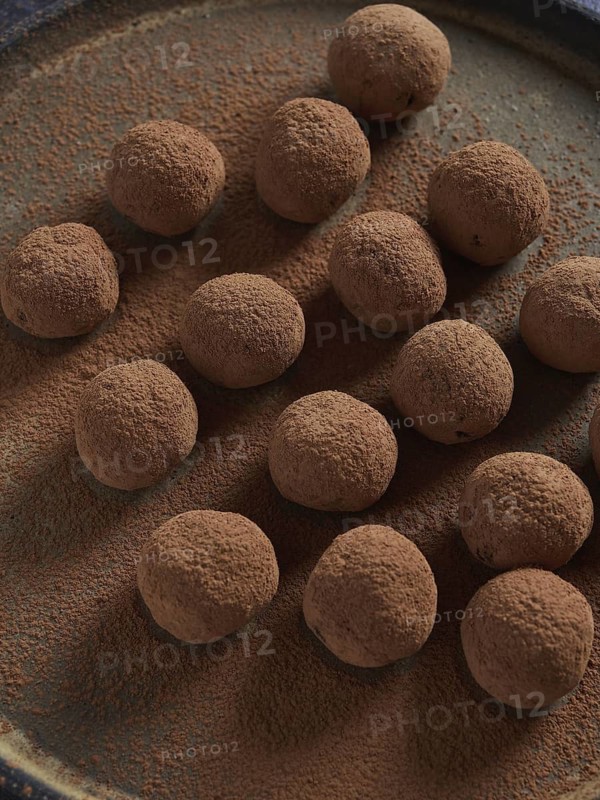 Healthy homemade raw treat, sugar free truffles made of dates, cocoa and nuts. Raw chocolate bliss balls dusted with cacao on a dark plate. Energy balls
