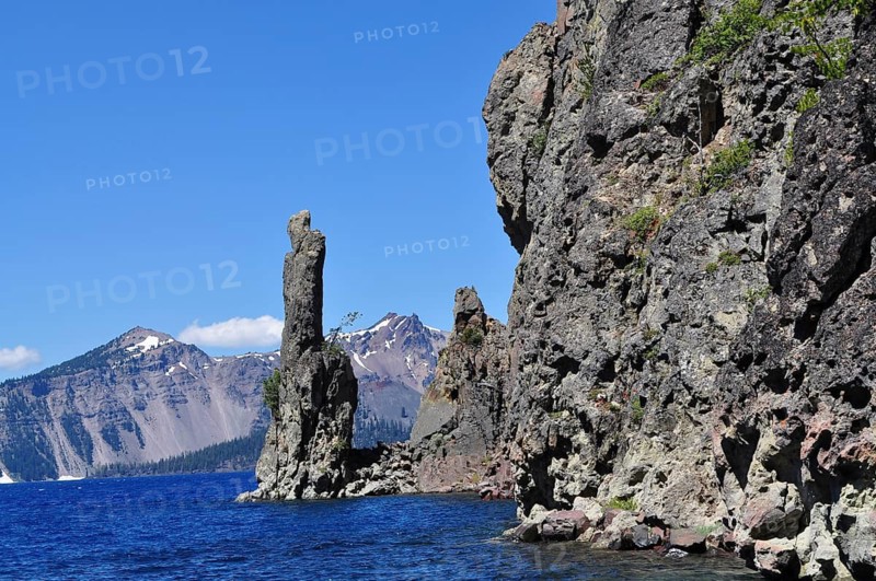Rocks at the edge of a lake with a mountain range in the background under clear sky, Crater Lake National Park, Oregon, USA