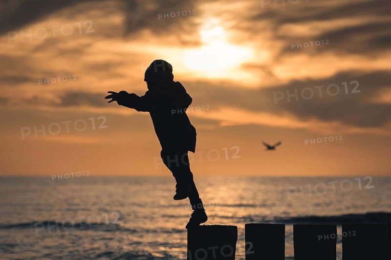 Silhouette of boy jumping from breakwater during sunset