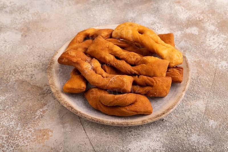 Crunchy biscuit Brushwood cookies sprinkled with powdered sugar on brown concrete background, side view, close up