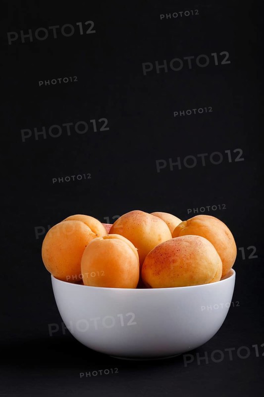 Fresh orange apricots in white bowl on black background. side view, copy space