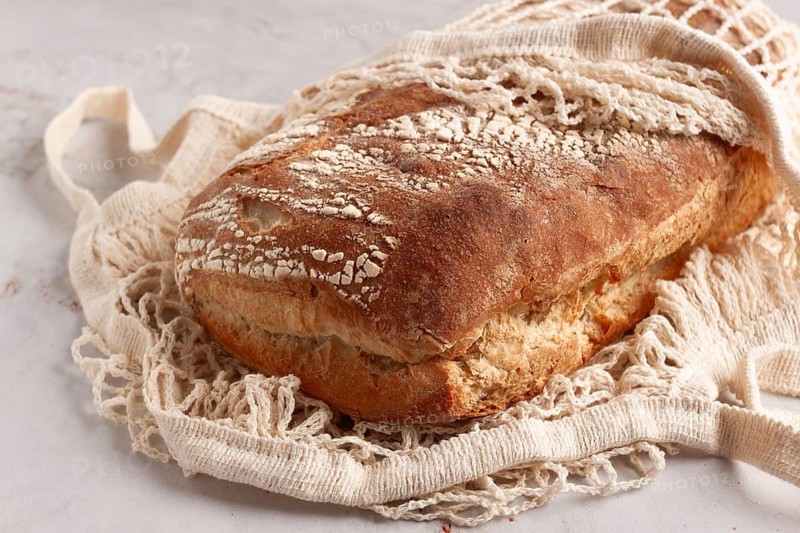Freshly baked rye bread, ciabatta, in a mesh bag, on a marble light table, natural light