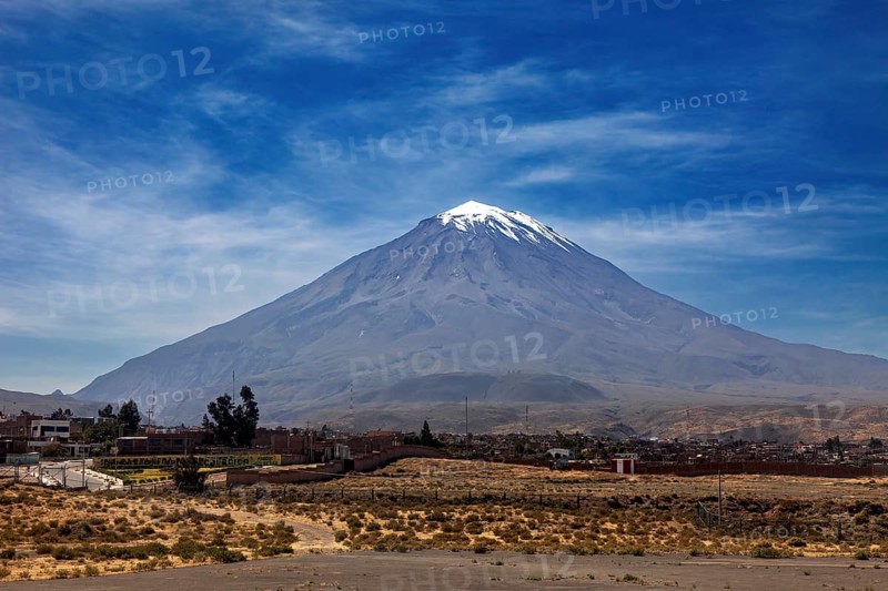 A snow-covered volcano rises majestically under a clear blue sky with light clouds, volcano in the Altiplano landscape near Arequipa in Peru