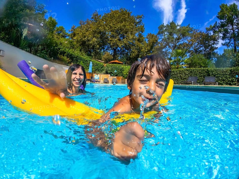 Mother and child enjoying active summer vacation, a boy splashing water from his mouth, swimming goggles creating water bubbles in a sunny outdoor pool