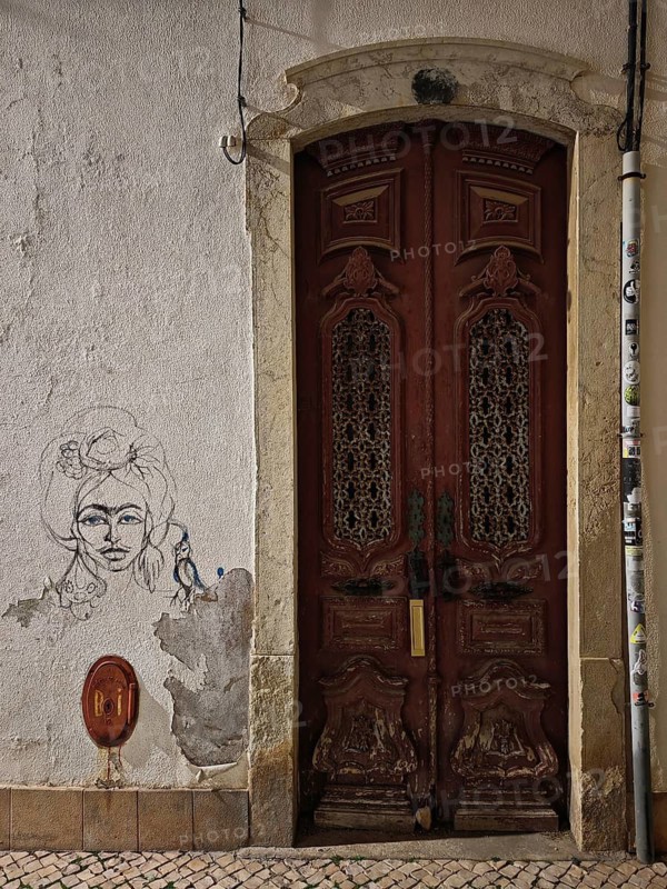 Framed wooden door with decorated relief, next to a portrait sketch on the wall, Lagos, Algarve, Portugal