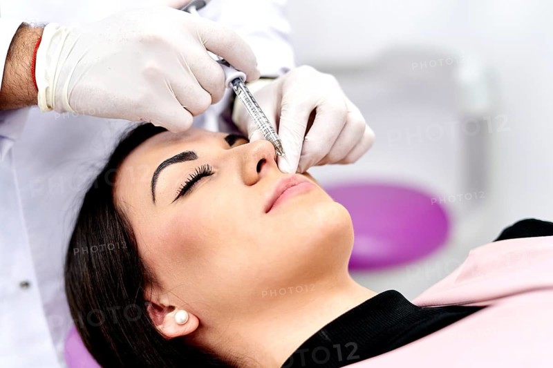 A woman receives a facial cosmetic surgery treatment in a clinical environment. A professional administers local anesthesia with precision and care, ensuring patient comfort