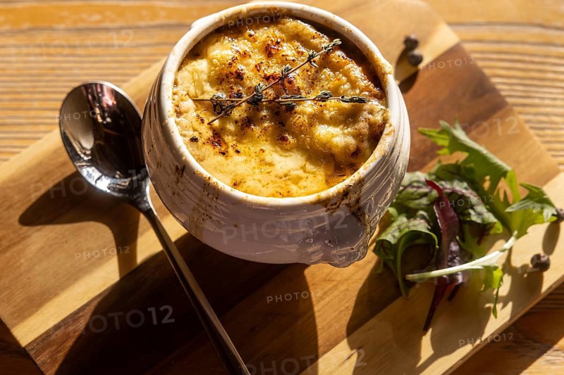 A sumptuous bowl of onion soup, topped with melted cheese and thyme, paired with a fresh side salad, presented on a rustic wooden board under natural lighting