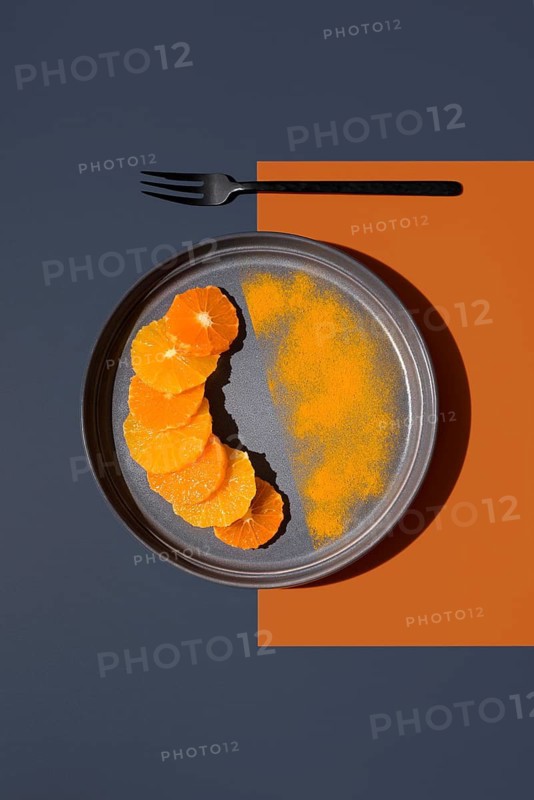 Sliced oranges and tangerines arranged on a gray plate with a contrasting orange and dark blue background. A fork lies above, creating a striking minimalist composition with vibrant colors
