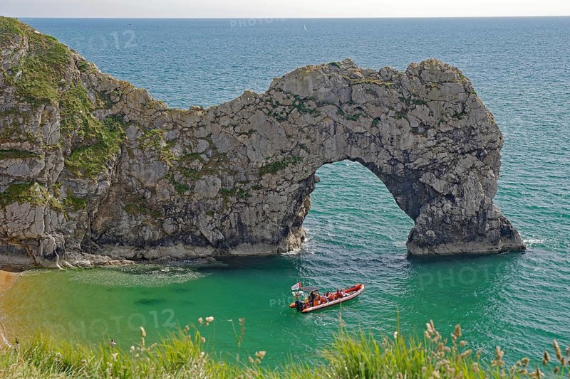 Boat in the turquoise blue sea in front of dramatic rock arches on the coast, Durdle Door, Weymouth, Dorset, England, United Kingdom