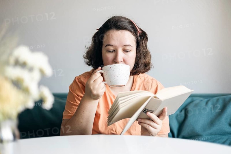 A woman enjoys a quiet moment at home, sipping coffee while reading a book. This cozy scene highlights relaxation and leisure
