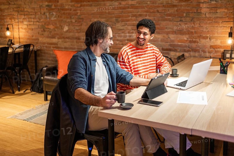 Two colleagues engage in a productive discussion at a coworking space. Laptops and coffee cups on the table emphasize a modern, collaborative work environment