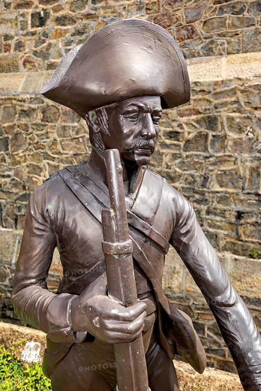 Bronze statue of a soldier in historic clothing in front of a stone wall, statue in the historic fortress of Galle in Sri Lanka