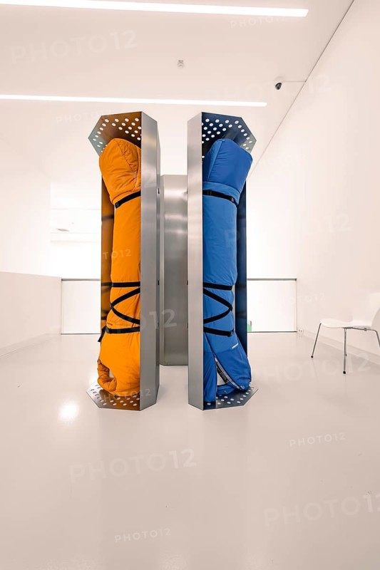 Two colourful, industrial pieces of luggage stand vertically in a white room, contrasting colours, Schauwerk Sindelfingen, Germany