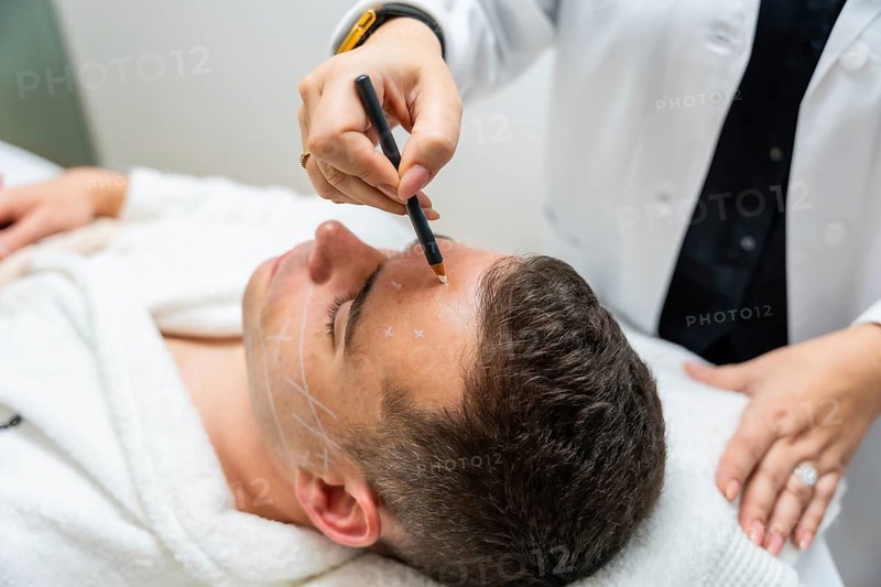 Doctor marking male patient's face with a pen for an upcoming cosmetic or plastic surgery procedure at an aesthetic clinic, focusing on skincare and beauty