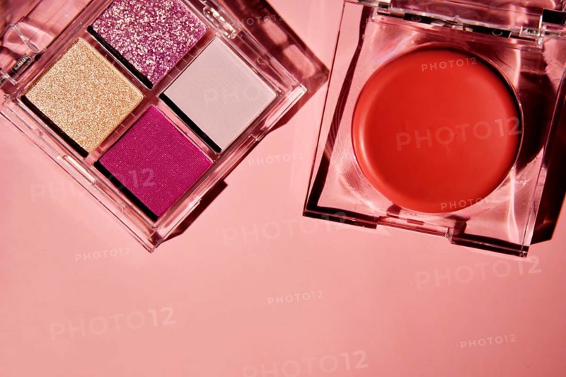 Top view of a vibrant makeup set featuring a pink eyeshadow palette with glitter and matte shades, accompanied by a blush compact on a soft pink background