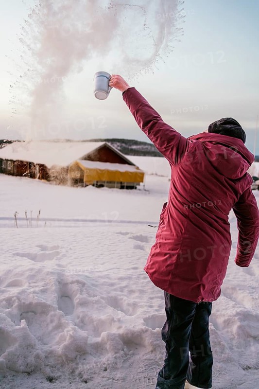 A person in a red coat throws water into the frigid air in Swedish Lapland, creating an impressive spray of ice crystals against the snow-covered backdrop