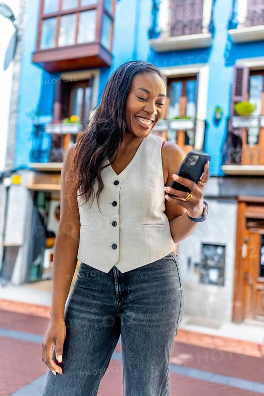 Happy businesswoman walking along a bustling city street, using her mobile phone to connect and engage with her network