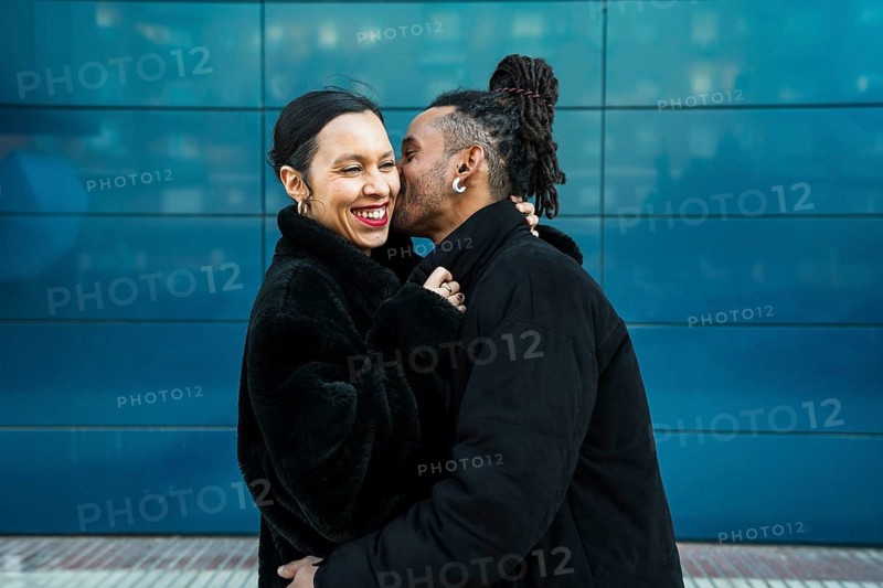A happy multicultural couple enjoys a tender moment outdoors, embracing love and diversity. The duo's attire blends modern style with traditional allure