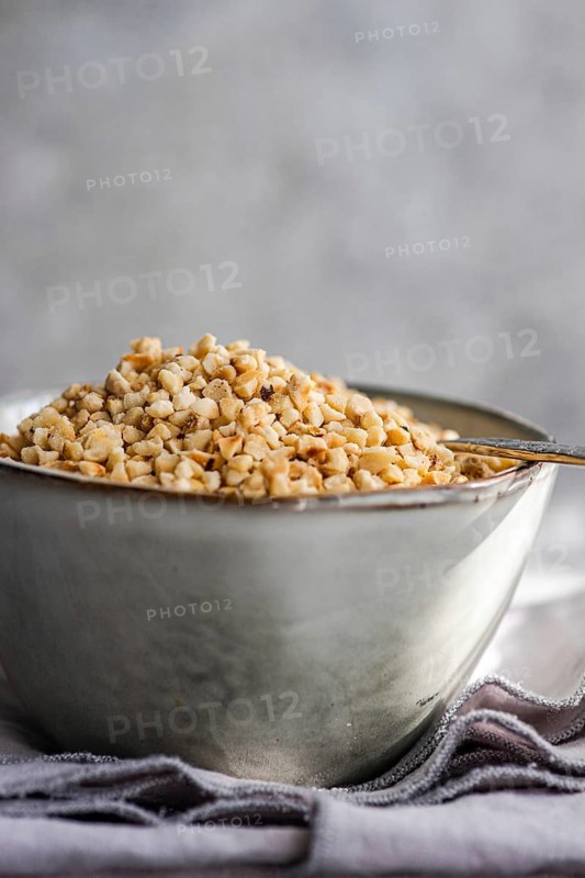 A bowl filled with chopped hazelnuts rests on a textured gray napkin, accompanied by an antique spoon