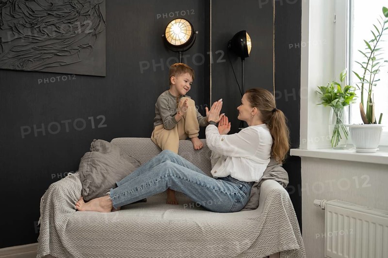 Mother and son share a joyful bonding moment on the couch, surrounded by cozy home decor. The boy is smile and mother is laughter capture a happy family scene