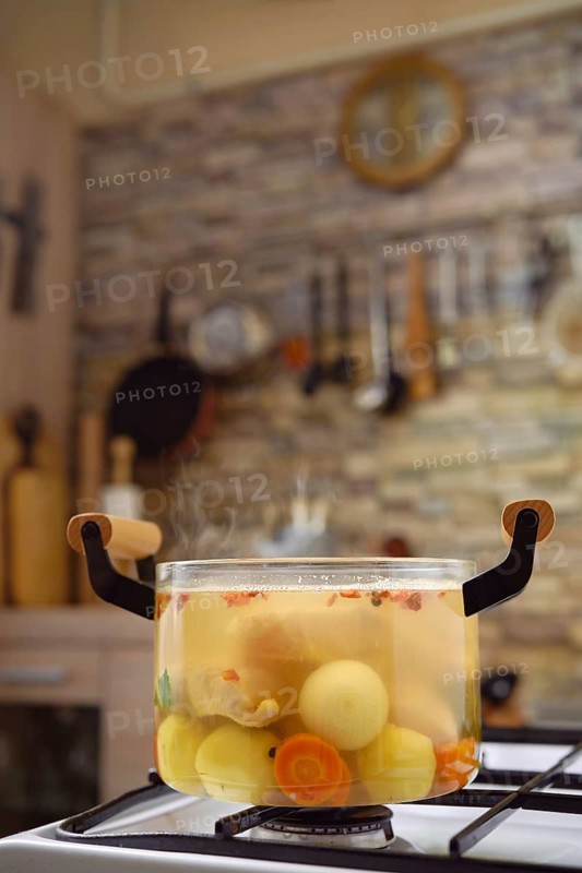 A pot filled with fresh vegetables and fish is simmering on the stove, releasing steam into a cozy kitchen. The warm atmosphere is enhanced by rustic decor and kitchen tools hanging nearby.
