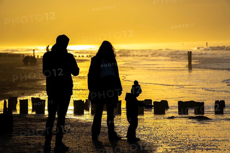 Winter on the North Sea, sunset at sea, beach walkers, coastal protection, through wooden posts, paalhoofden, on the beach, breakwater, the piles rammed into the sandy soil in double rows slow down the waves and ocean currents and thus slow down the flow rate of seawater, so less sand is washed away from the standing position, near Domburg, Walcheren peninsula in the Dutch province of Zeeland