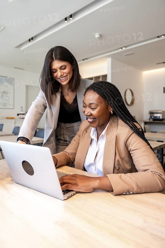Two businesswomen collaborating on a laptop, enjoying their business trip in a hotel, showcasing teamwork and productivity