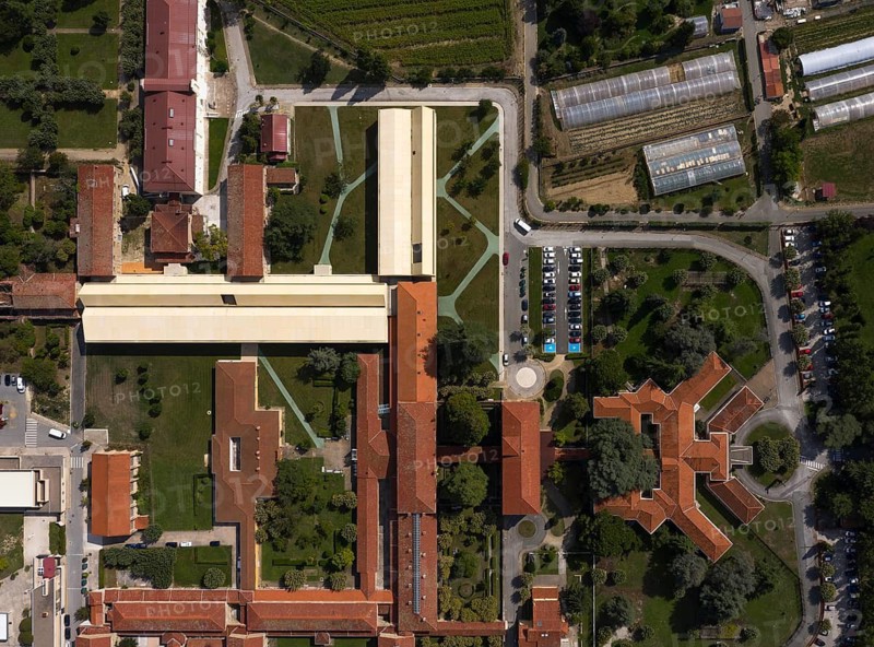 Aerial view of a large hospital with interconnected buildings surrounded by greenery, roads, and parking lots. The orderly design creates a harmonious urban landscape