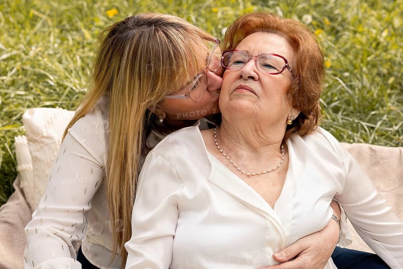 A touching moment between a mother and daughter enjoying time together in a sunny park. The daughter lovingly embraces and kisses her mother, highlighting their close bond
