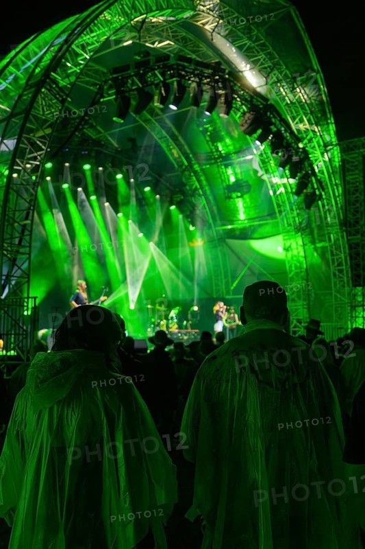 Audience in rain ponchos at a night concert in front of a green-lit stage, Klostersommer, Calw Hirsau, Black Forest, Germany