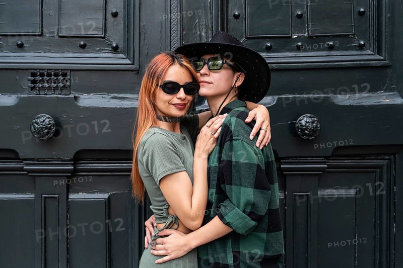 A Colombian lesbian couple embraces, showcasing pride and love against a rustic backdrop, symbolizing LGBTQIA+ diversity, respect, and identity
