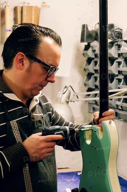 A skilled luthier focuses intently while assembling a bass guitar in a workshop, highlighting the precision and craftsmanship involved in this musical artistry