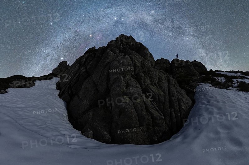A stunning view of the Milky Way over rugged rocks and snow in Iceland The silhouette of a lone figure adds scale, capturing the vastness of the northern night sky