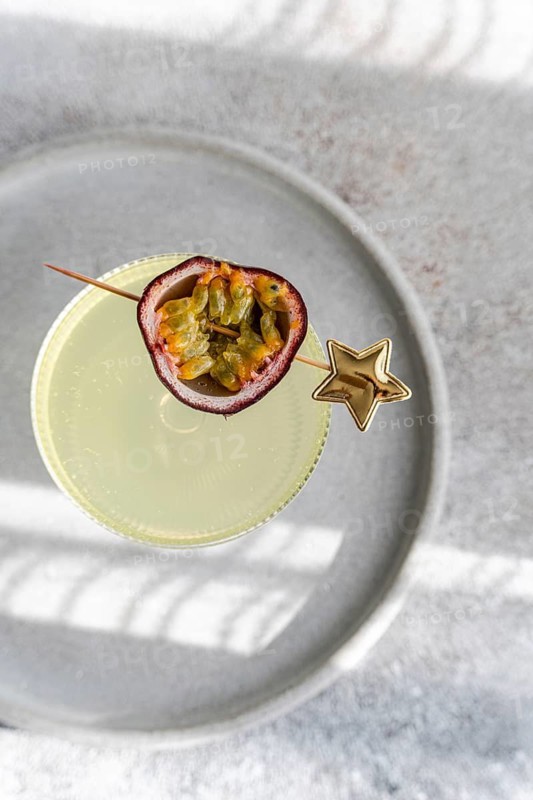 Top view of an elegant cocktail made with tonic, gin, and passion fruit juice, garnished with a half passion fruit placed on a circular plate, viewed from above