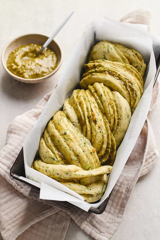 Ready to bake, homemade savoury babka plaited bread loaf flavoured with cheese and pesto, in the making tin
