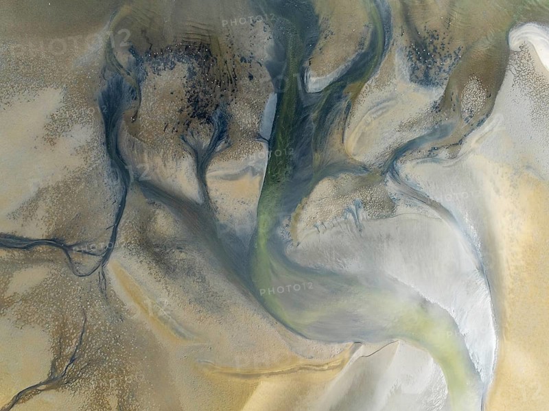 Streams and marshes at low tide in the wetlands of the Walvis Bay lagoon. In the distance Greater Flamingos (Phoenicopterus ruber). Aerial view. Drone shot. Walvis Bay, Namibia