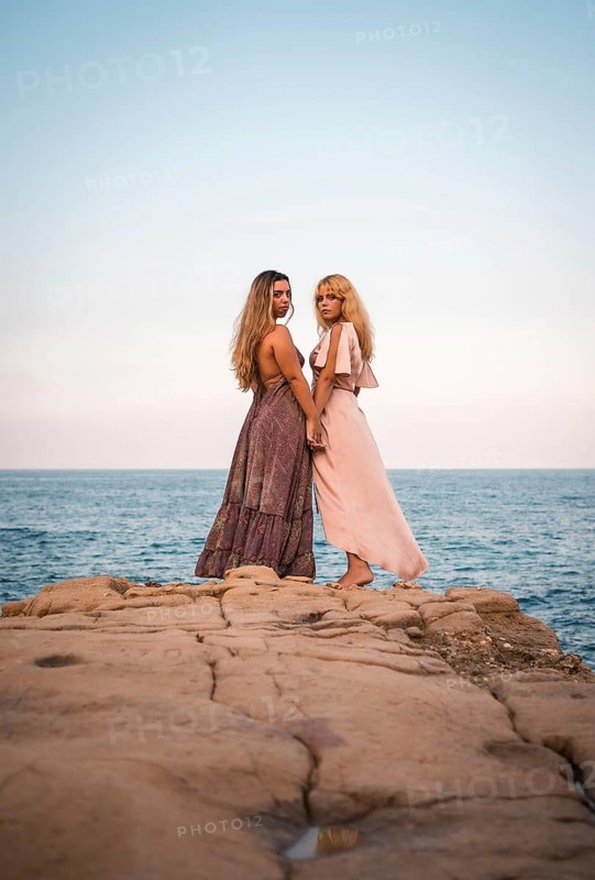 A couple of Caucasian girls with beautiful dresses, showing affection by the sea in summer