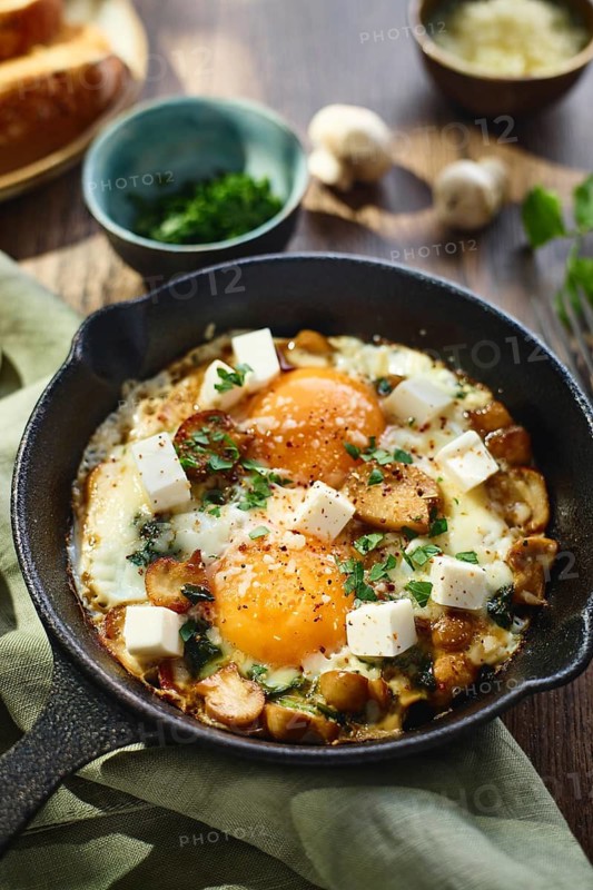 Fried eggs with spinach, mushrooms, grated cheese and feta cheese in small cast iron skillet, close up