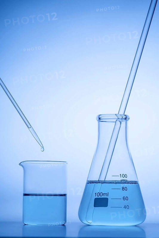 A laboratory beaker and flask filled with blue liquid, with a pipette dripping a drop in. The setup is illuminated with a soft blue light, giving a scientific atmosphere