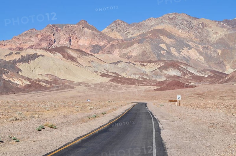 A lonely road crosses a dry desert landscape with imposing colorful mountains in the background, Artist Drive, Death Valley National Park, Mojave Desert, California, Nevada, USA
