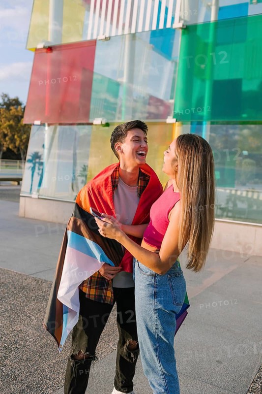 A joyful lesbian couple enjoys a sunny day wrapped in a pride flag, celebrating love and diversity. This inclusive scene embodies LGBTQIA+ pride and equality