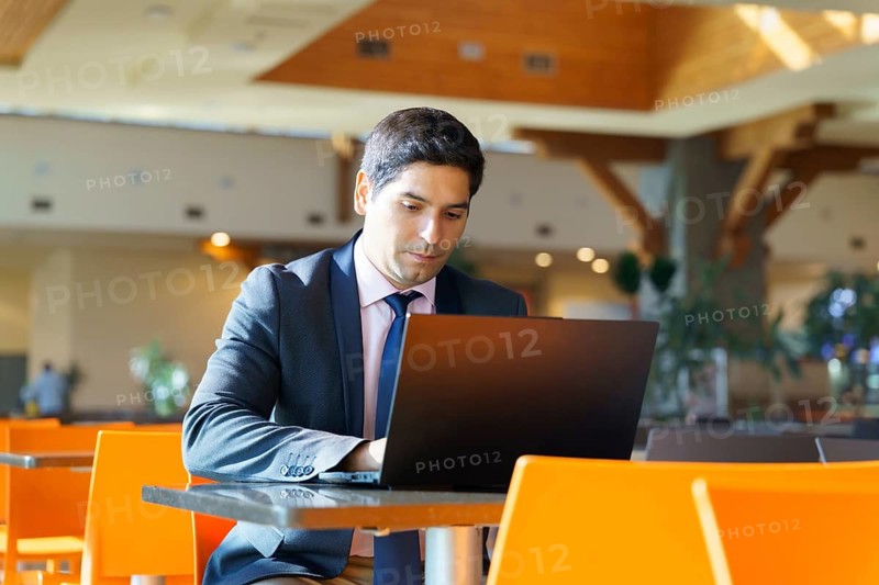 A focused young Chilean businessman working on his laptop in a modern cafe. He is dressed in a professional suit, highlighting his commitment and dedication to his work