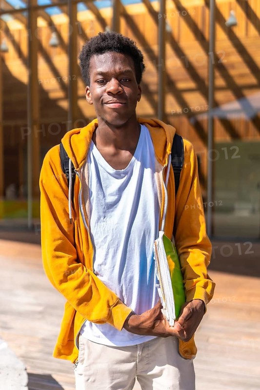 Vertical portrait of an african smiling student standing outside the university under the sun