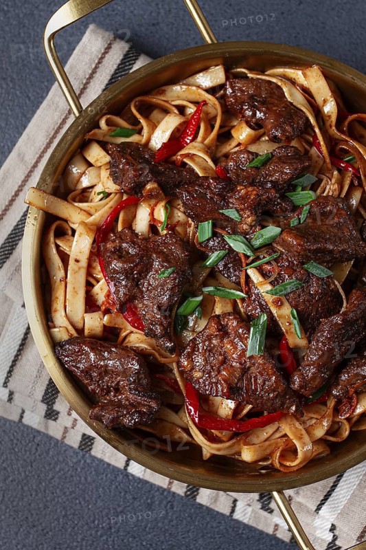 Udon noodles with Mongolian beef, green onions and vegetables, in a brass pan, on a gray background, homemade, no people