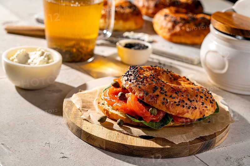 A freshly baked sesame seed bagel topped with smoked salmon, capers, and cream cheese on a rustic wooden board. A perfect snack for breakfast or brunch