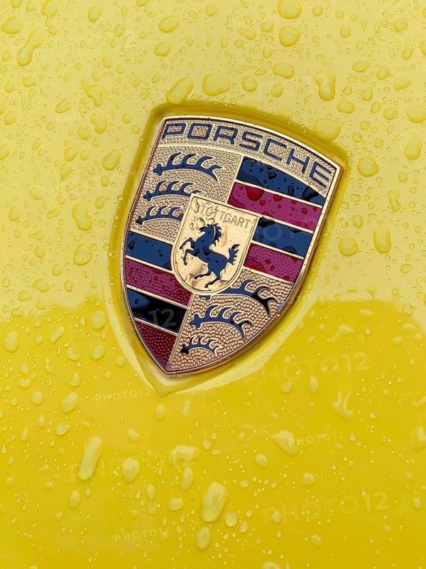 Porsche crest on yellow bonnet of sports car with sparkling raindrops, international